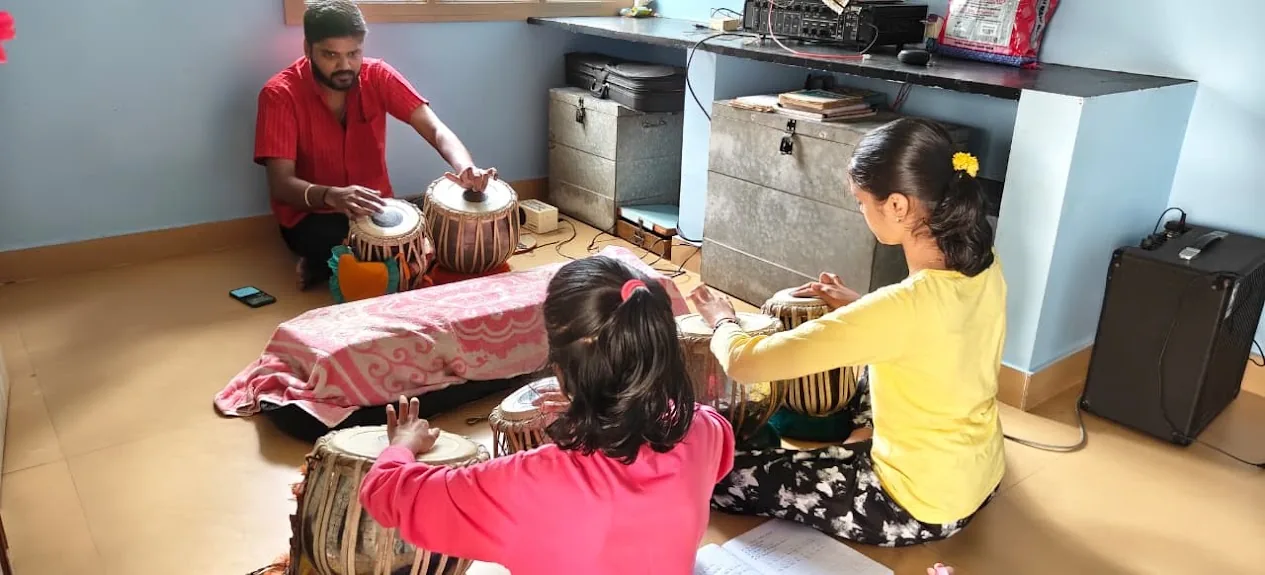 A teacher leads a tabla class as two young girls practise on their own pairs of tabla