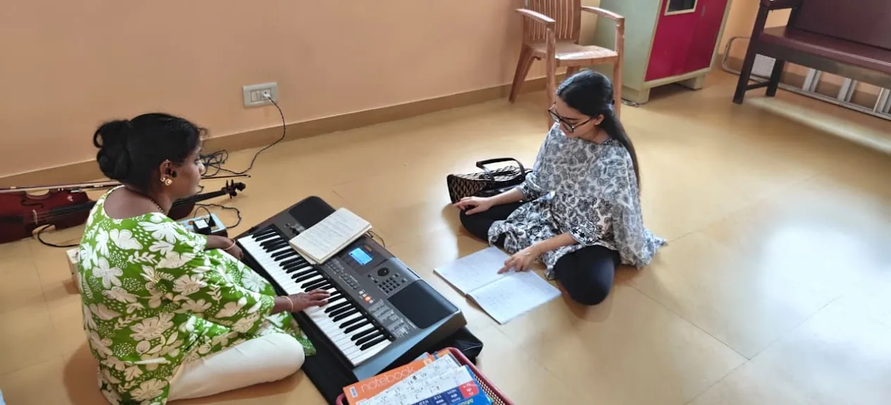 A teacher plays the keyboard while a student follows along in her notebook