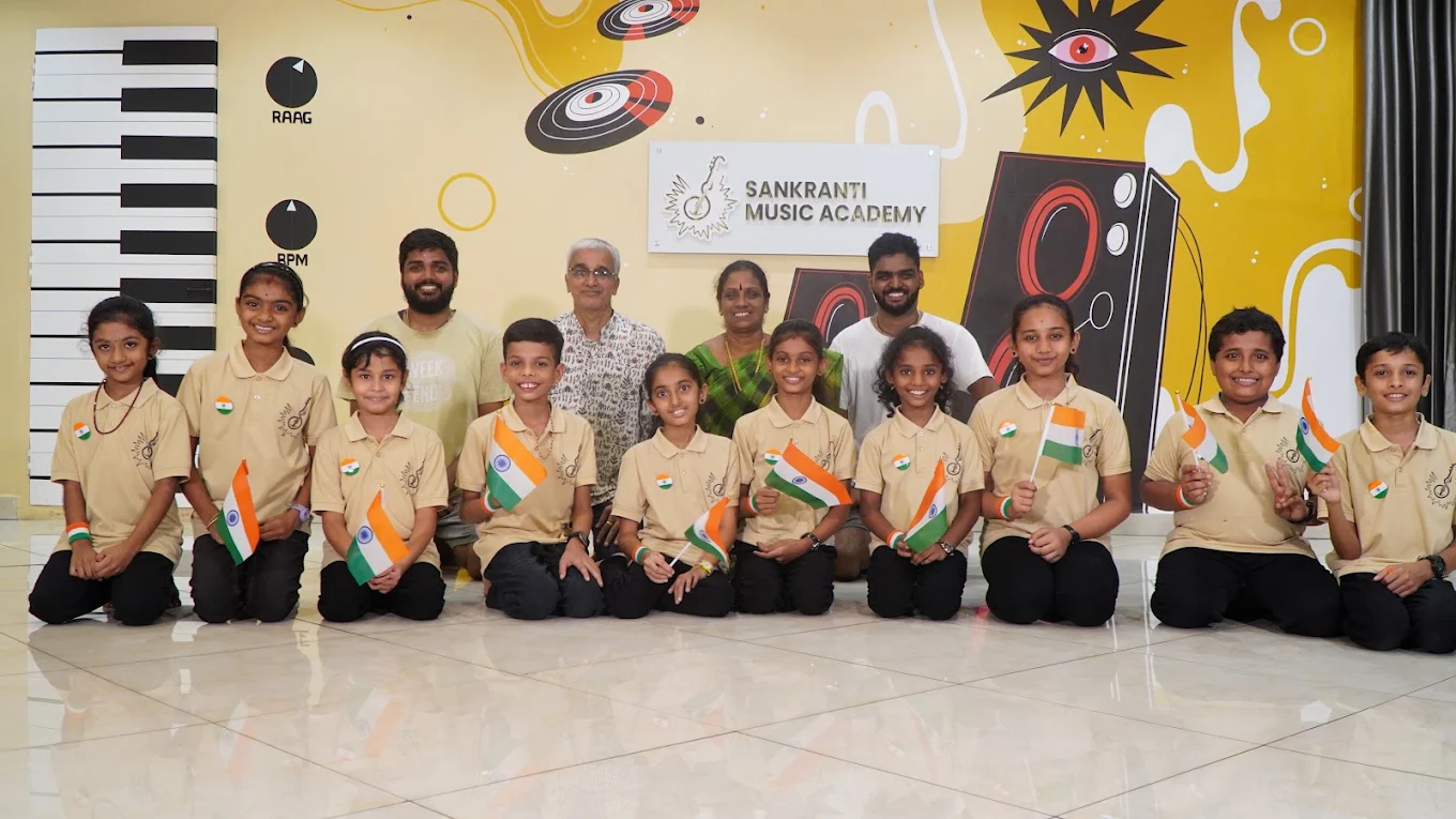Students in academy uniforms holding Indian flags with their teachers, in front of the Sankranti Music Academy sign